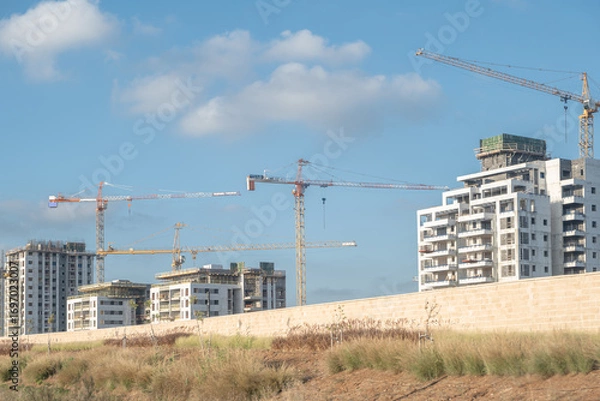 Fototapeta building is under construction, with a prominent crane towering over the site. The scene represents modern real estate development in Israel,  new arch housing  projects.