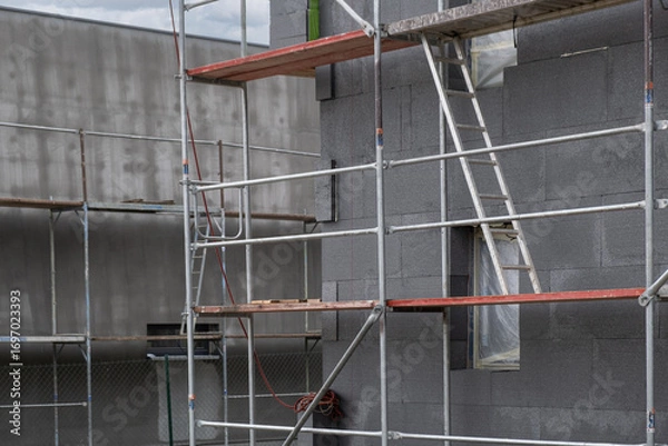 Fototapeta building under construction shows a facade covered in dark gray insulation panels. scaffolding.