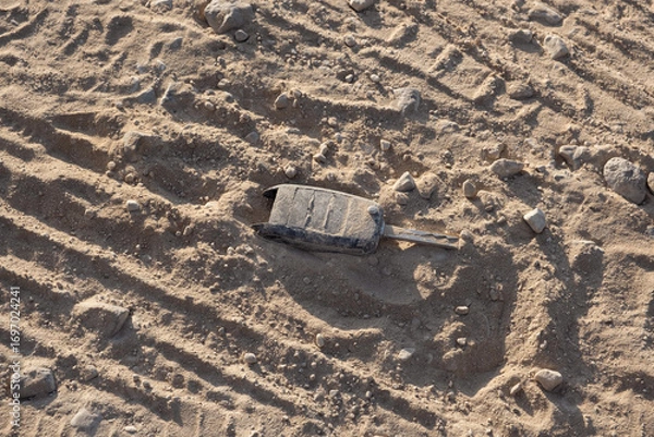 Fototapeta Lost Car Key on Sandy Road. Damaged car key lies on sandy road with multiple intersecting tire tracks pressing into loose sand around the key