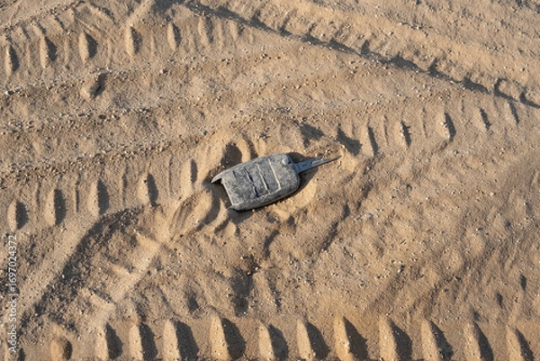 Fototapeta Lost Car Key on Sandy Road. Damaged car key lies on sandy road with multiple intersecting tire tracks pressing into loose sand around the key