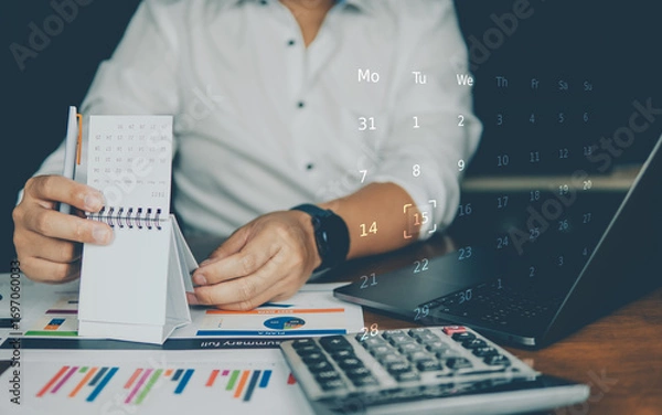 Fototapeta A person in business attire writes on a notepad with charts, a laptop, and calculator, overlaid with futuristic digital data.