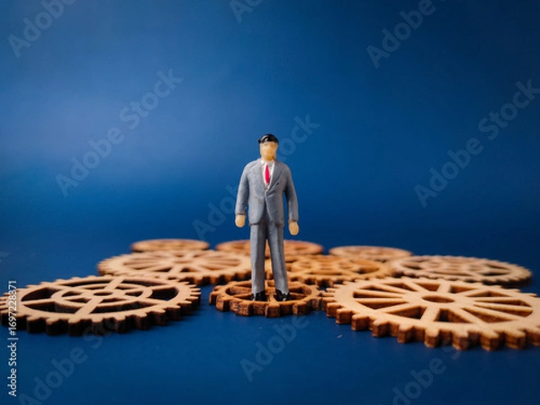 Fototapeta The image of a miniature businessman standing on wooden gears can symbolize various aspects of business and work