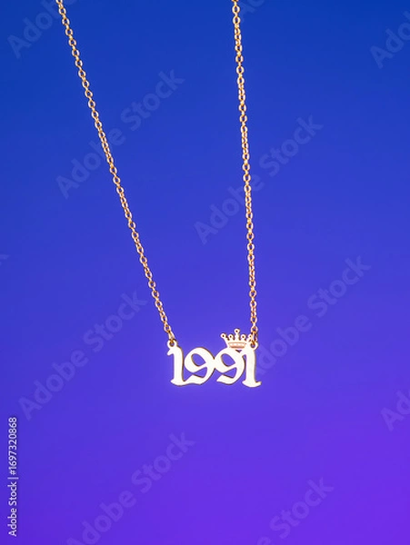 Fototapeta Close-up of a metallic gold pendant in the shape of "1991" on a chain, on a  purple background