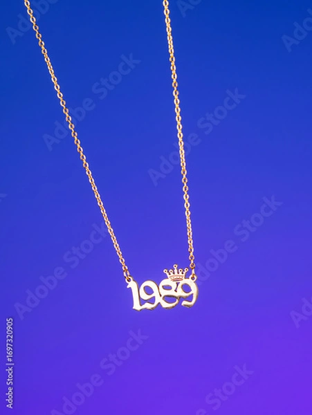Fototapeta Close-up of a metallic gold pendant in the shape of "1989" on a chain, on a  purple background