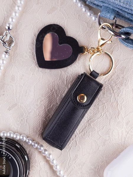 Fototapeta Close-up of a black  leather lipstick case with a heart-shaped mirror, elegantly placed on a lace table decorated with jewelry and ornaments