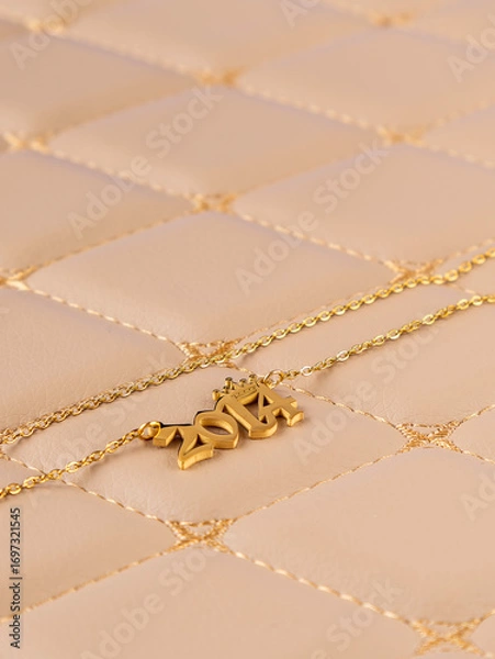 Fototapeta Close-up of a metallic gold pendant in the shape of "2014" on a chain, on a beige leather background