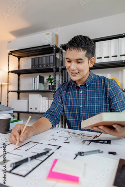 Fototapeta Young architect working in office with building models and floor plans, analyzing details and creating innovative design concepts, showing creativity, focus, and dedication in architecture projects.