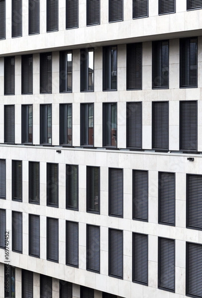 Fototapeta Contrasting dark windows in white concrete building wall