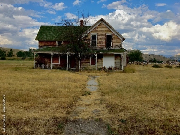 Fototapeta Old abandoned wood clapboard farmhouse with blue sky and clouds. 