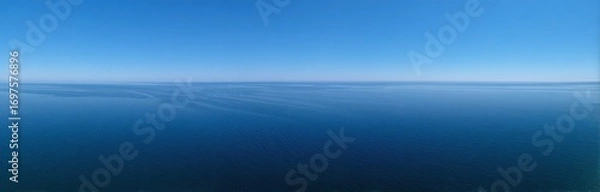 Fototapeta Serene vista of a calm, deep blue ocean under a clear azure sky, with a faint, hazy horizon line separating the two tranquil expanses