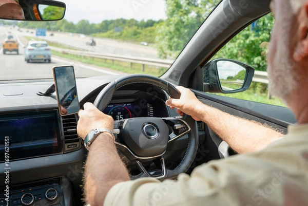 Fototapeta Driving on a sunny day with the hands on the steering wheel and mobile phone mounted for navigation and updates on a highway in the countryside