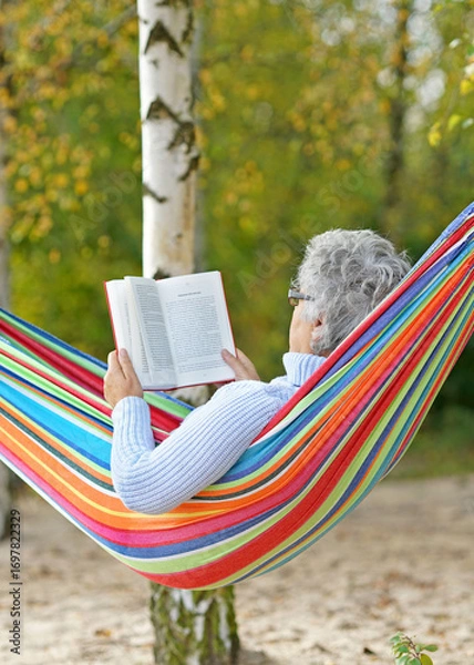Fototapeta Relaxed Senior woman Reading in a Hammock by the Lake in Autumn