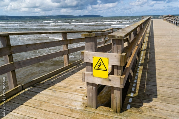 Fototapeta Enjoy a scenic wooden pier that features a caution sign, all while overlooking the sea