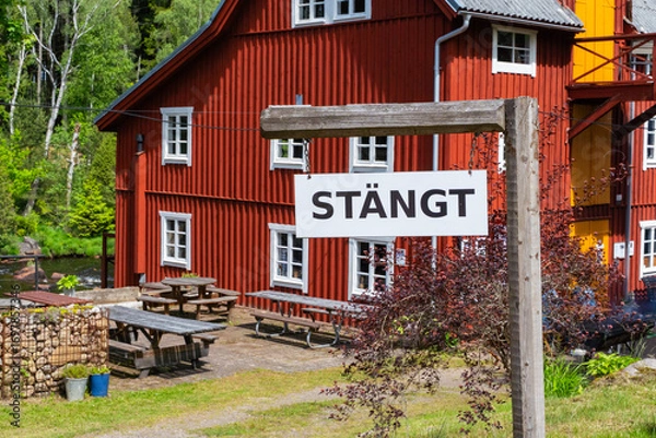 Fototapeta A sign reading CLOSED in front of a picturesque red wooden building in a serene outdoor setting, Sweden