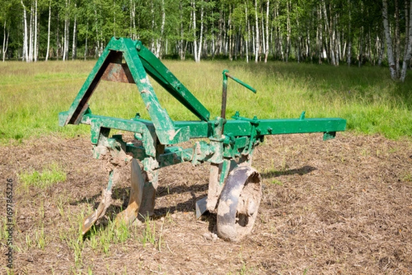 Fototapeta A tractor trailer plow stands in an agricultural field on a summer day
