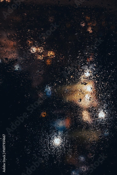 Fototapeta Rainy Night Cityscape Through Wet Window with Cinematic Bokeh. Rain-covered window, with dense droplets and streaks creating a textured foreground. Blurred city lights in the background.