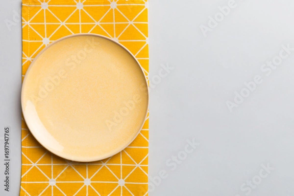 Obraz Top view on colored background empty round yellow plate on tablecloth for food. Empty dish on napkin with space for your design