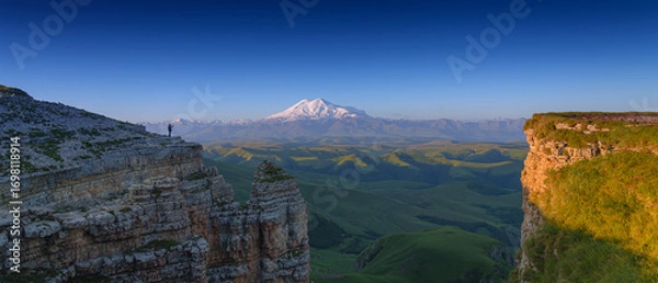 Fototapeta panoramic view of the Bolshoy Bermamyt plateau, with the snow-capped peaks of Mount Elbrus in the background, in early morning, at daytime, Stavropol Krai, Russia