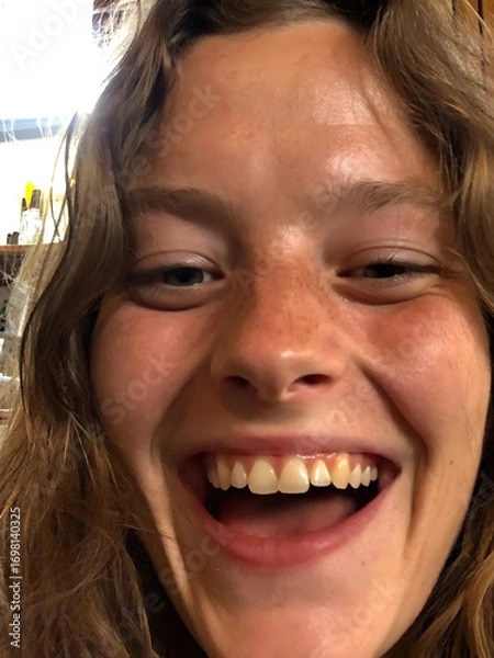 Fototapeta Smiling young woman enjoying a moment of joy indoors in a cozy setting with natural lighting and warm colors
