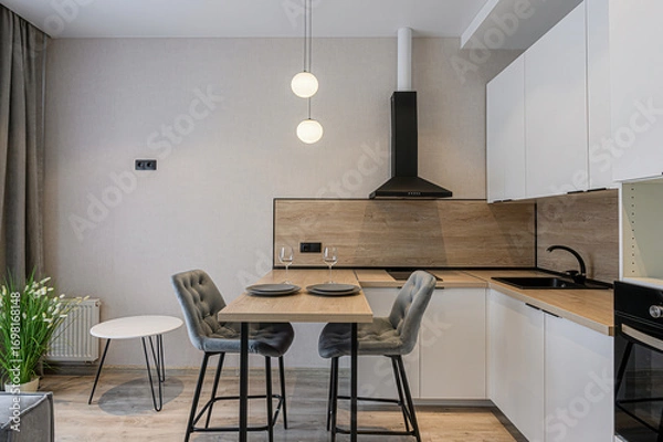 Fototapeta modern kitchen with white cabinets, a wooden backsplash, and a small dining area featuring two gray chairs, a wooden table set for two, and pendant lighting