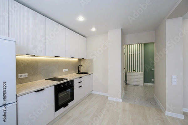 Fototapeta modern kitchen with white cabinets, a stone countertop, and black fixtures. An open hallway leads to a green-accented room