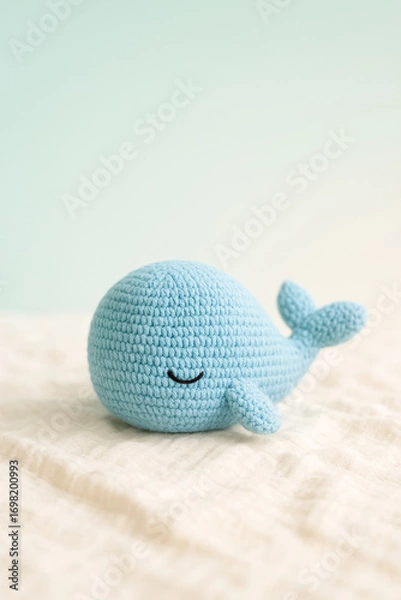 Fototapeta Close-up of a charming blue crochet whale toy resting on soft white fabric with a simple, pastel background, evoking a sense of craftsmanship, coziness, and playful charm.