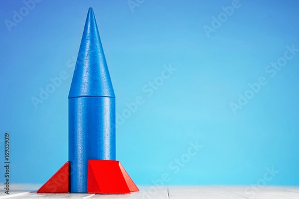 Fototapeta Abstract blue rocket from wooden blocks with copy space. Wooden puzzle in rocket shape, start up concept.