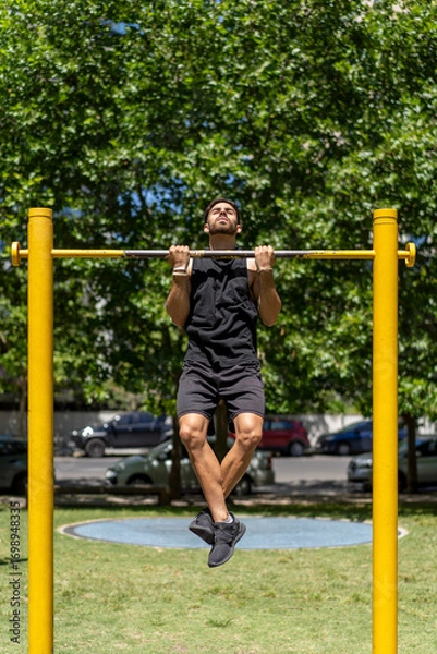 Fototapeta Fit young man executing pull-ups in a park setting