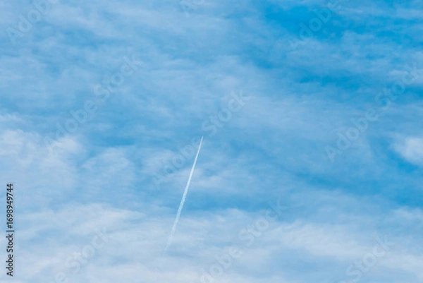 Fototapeta Trace of a flying airplane in the blue sky with soft white fluffy clouds background