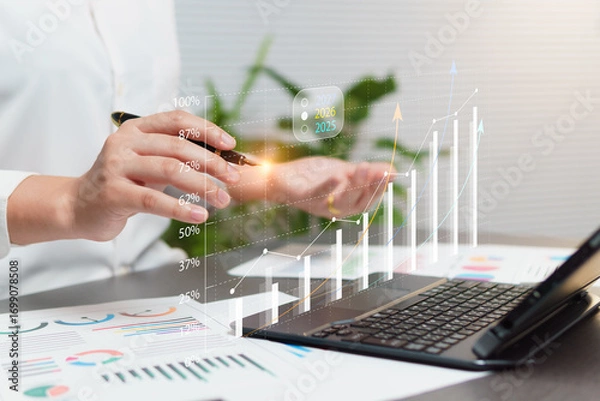Fototapeta 2025-2026 Marketing Strategy Analysis Concept, Business Growth Assessment with Graphs and Documents, woman Working in Office and Having Tablet on Desk with Virtual Graph Icons and Touch Pen Tip