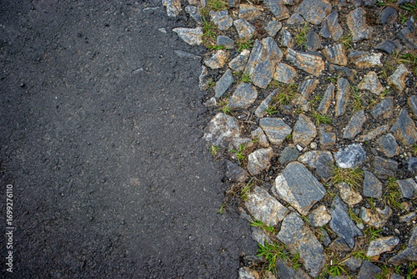 Obraz detail of irregular cobblestone street with grass growing between the stones with a section covered in new asphalt