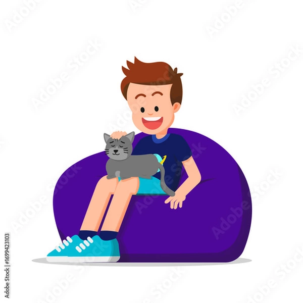 Fototapeta A boy sits on a beanbag with a sleeping cat on his lap