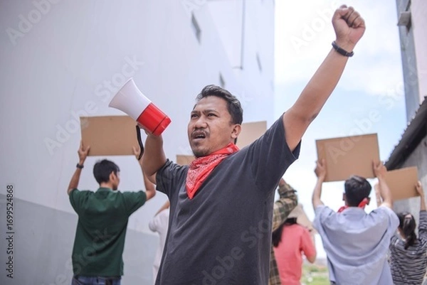 Fototapeta Asian Male Activist Using Megaphone To Amplify Voice And Raising Hands While Leading Group