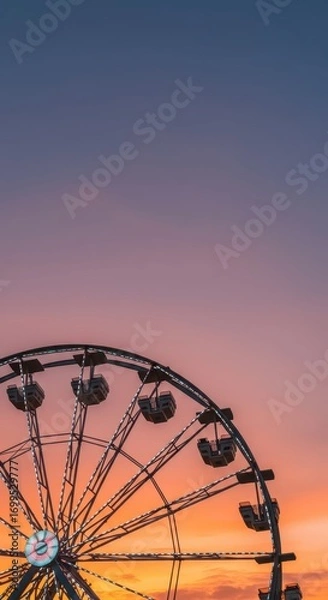 Fototapeta A magnificent Ferris wheel stands tall against a vibrant sunset sky, showcasing a captivating display of warm colors and intricate details.
