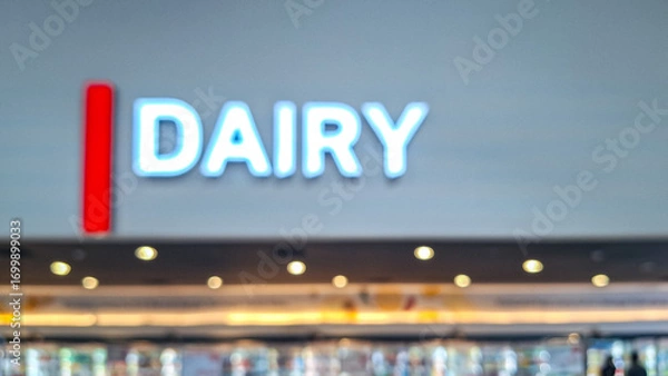 Fototapeta Blurred background of a signage of "DAIRY" in a wall in a prominent and glowing font indicating a section in a store or a product category within a grocery store or supermarket. 