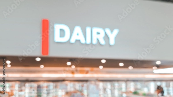 Fototapeta Blurred background of a signage of "DAIRY" in a wall in a prominent and glowing font indicating a section in a store or a product category within a grocery store or supermarket. 