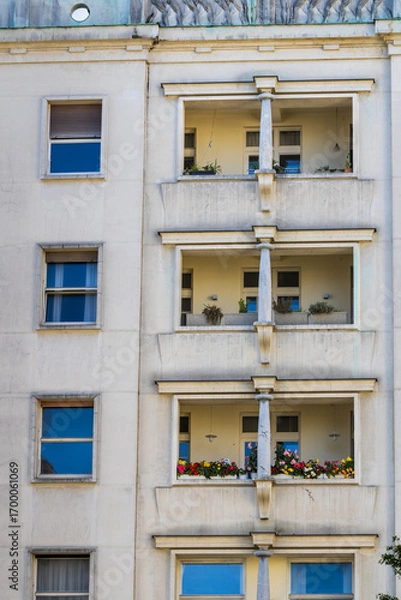 Fototapeta facade of a building, Four-story building facade with balconies, plants, and open windows