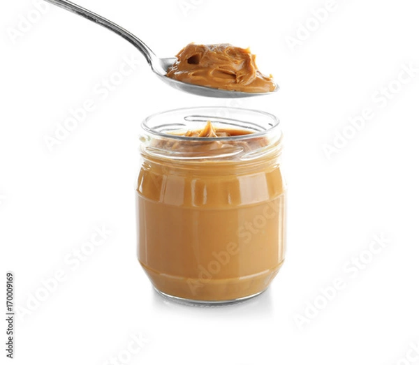 Fototapeta Creamy peanut butter in spoon and jar on white background