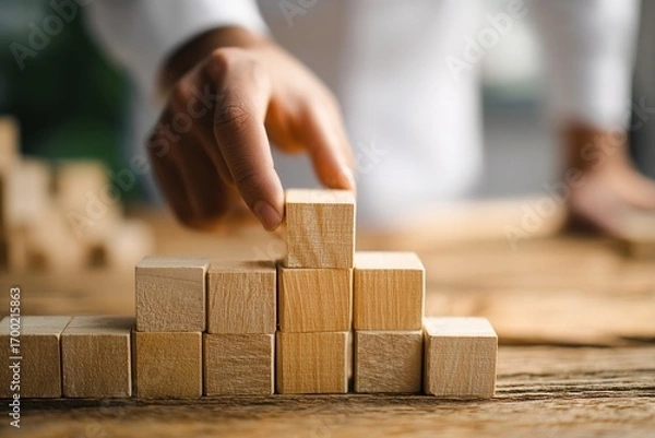 Fototapeta business man try to build wood block on wooden table and blur background business startup concept. High quality