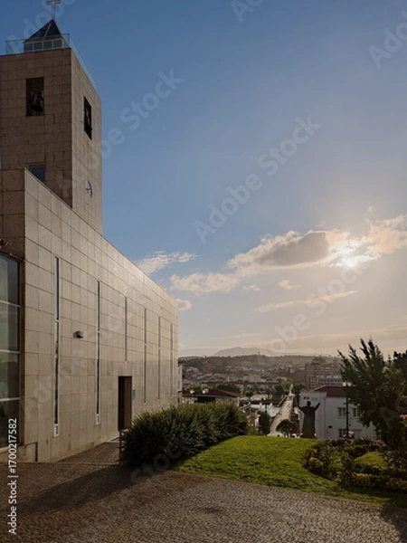 Fototapeta Partial view of the modern church tower and facade in Mirandela, Portugal, with a panoramic cityscape and sunset sky, capturing local faith, architecture, and urban life in a tranquil evening scene.