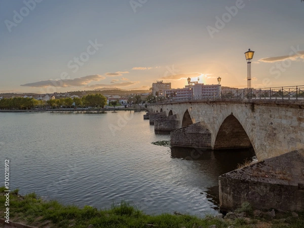 Fototapeta Stone bridge over the Tua River in Mirandela, Portugal, with granite arches and pedestrian use. August 2025, peaceful historic landmark connecting old city sides.