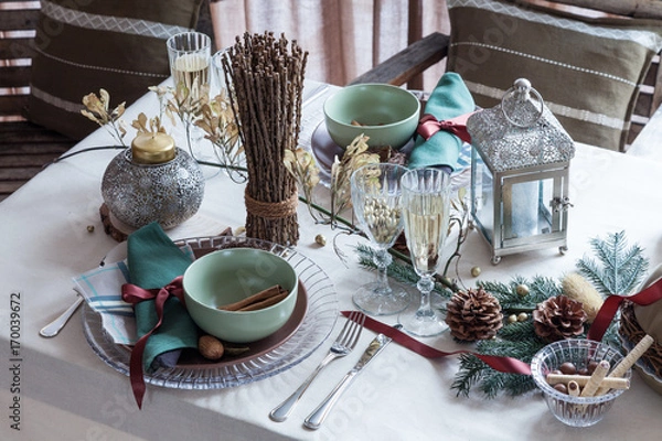 Fototapeta Holiday served table with tablecloth, wineglasses, plates, cones, candeles and sweets in restaurant. Festive table for two persons with champagne in glasses. Dinner party, winter style.