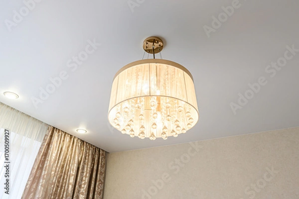Fototapeta Elegant drum chandelier with crystal beads hanging from a fabric shade, ceiling spotlights, and decorative curtains