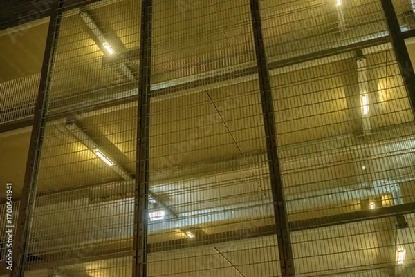 Fototapeta Metal mesh grid protecting building floors with lights shining through