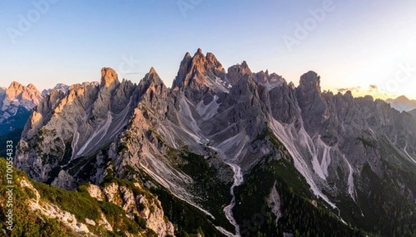 Fototapeta Panoramic view of snow-covered mountains at sunset, with golden light casting dramatic shadows across rugged peaks and valleys, evoking serenity, elevation, and the sublime beauty of winter.