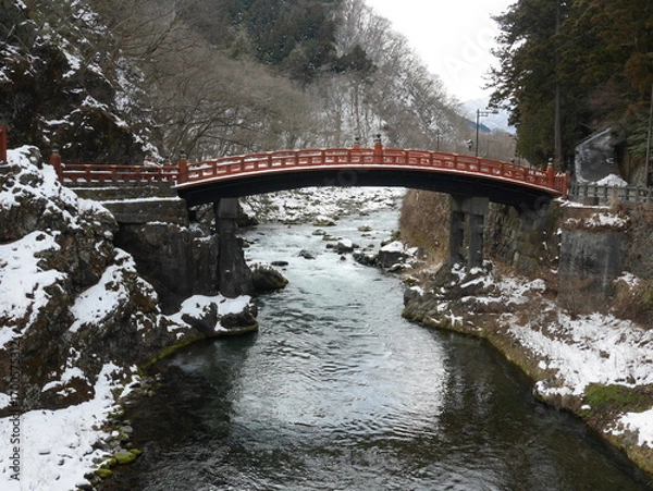 Fototapeta Scenic Red Bridge Over Serene River Surrounded by Snowy Landscape