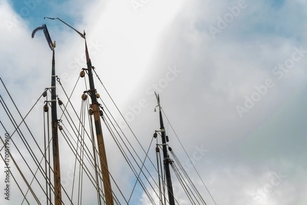 Fototapeta Wooden masts of a sailboat with rigging and pennant waving in the wind