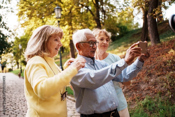 Fototapeta Joyful older adults happily taking a fun selfie together in a beautiful autumn park setting