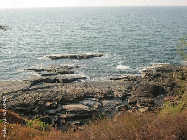 Fototapeta Rocky coastline with ocean waves and distant horizon in daylight  