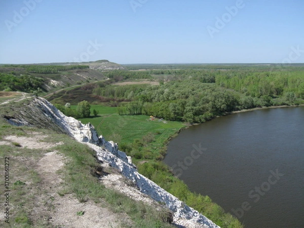 Fototapeta Scenic river view with lush greenery and cliff under blue sky  